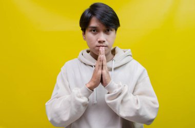  Düşünceli, kafası karışmış Asyalı bir adam sarı arka planda izole edilmiş bir şey seçip seçmeyeceğini düşünüyor.