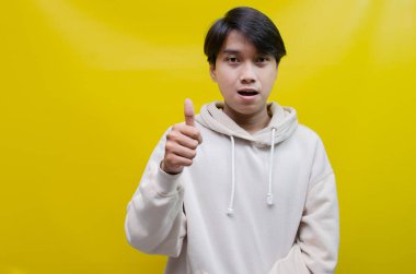 Reklam ve ürün yerleştirme kavramları için mutlu, gülümseyen Asyalı genç bir adam avuçlarını açar ve uzayı kopyalamak için işaret eder.