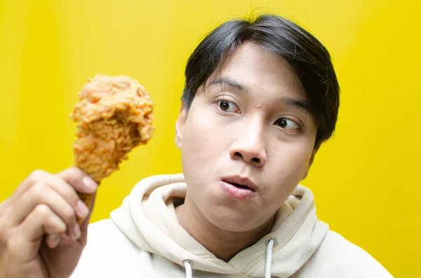 Happy surprised asian man holds fried chicken with wow expression isolated over yellow background. unhealthy food concept. food sale promotion