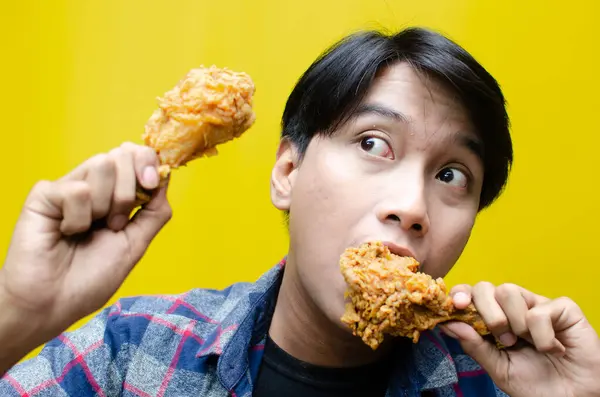 Happy surprised asian man holds fried chicken with wow expression isolated over yellow background. unhealthy food concept. food sale promotion