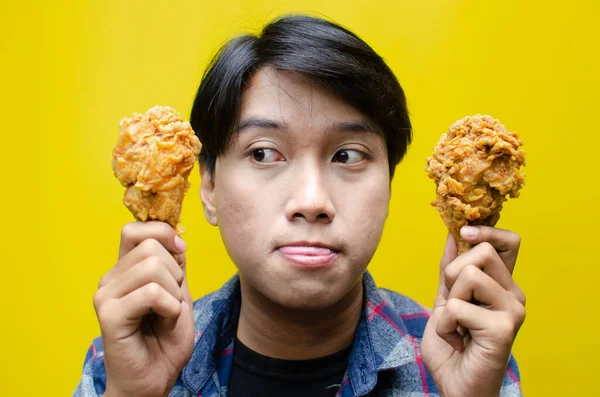 Aç adam sarı arka planda kızarmış tavuk tutuyor.