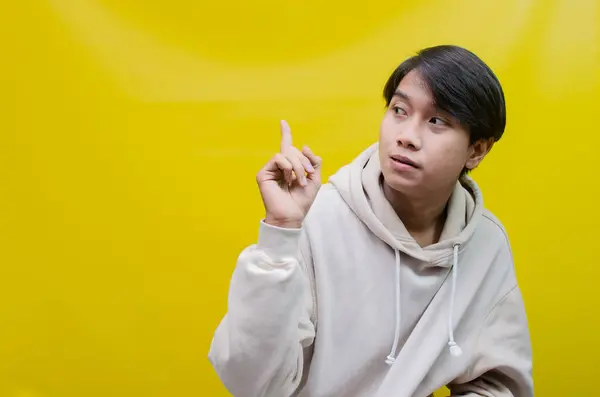 Reklam ve ürün yerleştirme kavramları için mutlu, gülümseyen Asyalı genç bir adam avuçlarını açar ve uzayı kopyalamak için işaret eder.