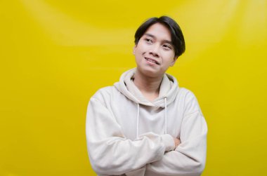 Düşünceli, kafası karışmış Asyalı bir adam sarı arka planda izole edilmiş bir şey seçip seçmeyeceğini düşünüyor.