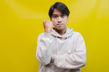 Bej kapüşonlu Asyalı adam mutlu bir şekilde dans ediyor ve sarı arka planda zaferini kutluyor. 