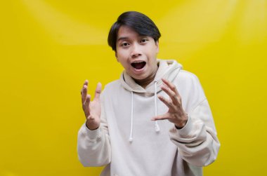 Bej kapüşonlu Asyalı adam mutlu bir şekilde dans ediyor ve sarı arka planda zaferini kutluyor. 