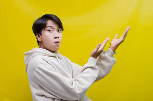 Bej kapüşonlu Asyalı adamın yan görünüşü parmaklarını uzatıp kollarını açarak iyi bir şey tanıtmak ve reklamını yapmak için.