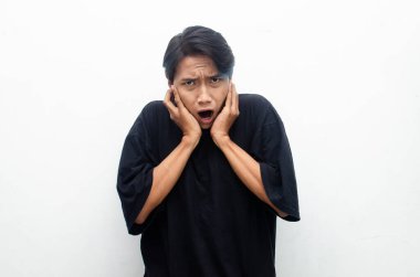 Histerik, bunalımlı Asyalı genç adam kulaklarını eliyle kapatıyor, bağırıyor ve çığlıklar atıyor beyaz arka planda izole bir şekilde.