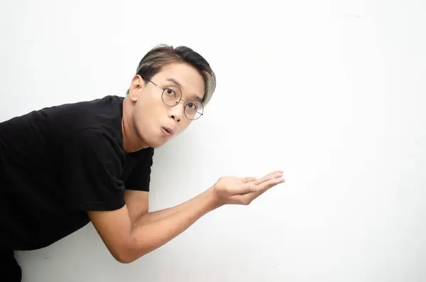 Siyah tişört giyen Asyalı genç bir adamın portresi. Heyecanlı görünüyor ve beyaz arka planda izole edilmiş bir şey gösteriyor.   