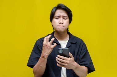 Asyalı sinirli genç adam akıllı telefonunu kullanıyor. 