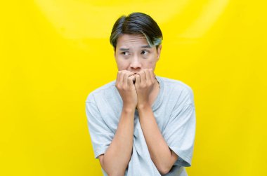 Asyalı genç adamın portresi endişeli görünüyor. Sarı arka planda tırnaklarını yiyor.  