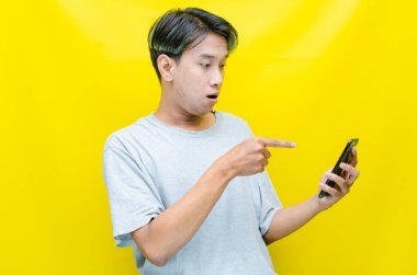 Yong Asyalı adam sarı arka planda telefonunu kullanıyor. 