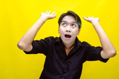 Asyalı genç bir adamın portresi sarı arka plandaki bir şeyi işaret ediyor.   