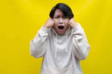 Sarı arka planda bağıran Asyalı genç adam. 