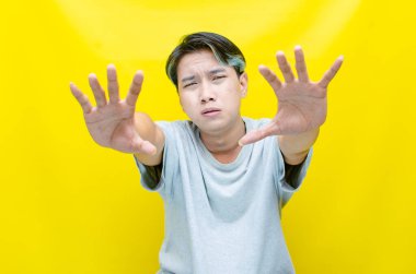 Asyalı üzgün bir adamın portresi. Sarı arka planda ellerini gösteriyor.   