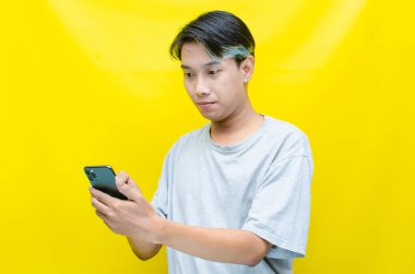 Sarı arka planda akıllı telefonu olan genç Asyalı bir adam. 