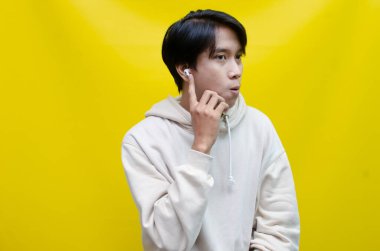 Bej kapüşonlu mutlu, kendini ifade eden Asyalı adam kablosuz kulaklıklarla müzik dinliyor.