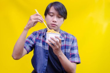 Asyalı adam sarı arka planda lezzetli eriştelerden hoşlanıyor. 