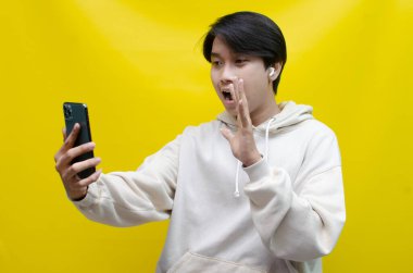 Yong Asyalı adam sarı arka planda telefonunu kullanıyor. 