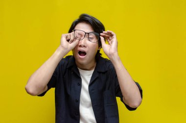 Siyah tişörtlü genç Asyalı adam sarı arka planda gözlük takıyor.. 