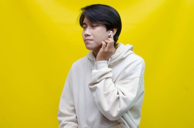 Bej kapüşonlu mutlu, kendini ifade eden Asyalı adam kablosuz kulaklıklarla müzik dinliyor.