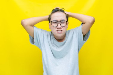 Sarı arka planda stresli Asyalı genç adam 