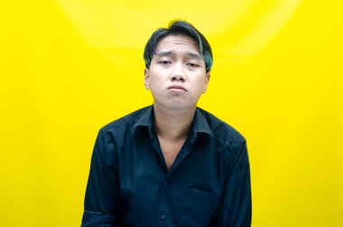 Sarı arka planda poz veren bitkin ve üzgün Asyalı bir adamın portresi..