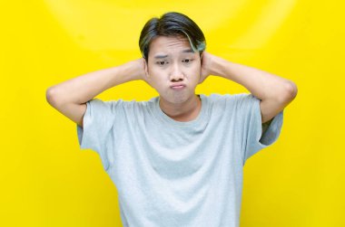 Sarı arka planda poz veren umutsuz Asyalı genç bir adamın portresi..