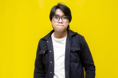 Sarı arka planda gözlüklü düşünceli genç Asyalı adam.