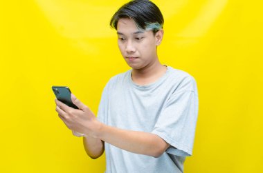 Sarı arka planda akıllı telefonu olan genç Asyalı bir adam. 