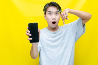 Sarı arka planda akıllı telefonu olan genç Asyalı bir adam. 