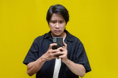 Asyalı sinirli genç adam akıllı telefonunu kullanıyor. 