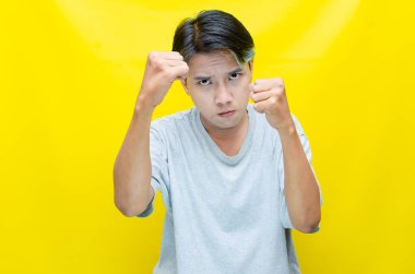 Asyalı beyaz tişörtlü bir adamın portresi. Kızgın yüzü sarı arka planda izole edilmiş.