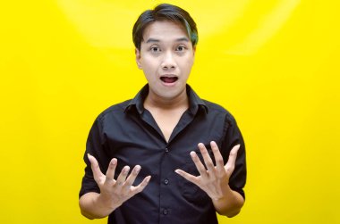 Siyah tişörtlü genç Asyalı adam sarı arka planda şok olmuş görünüyor.. 