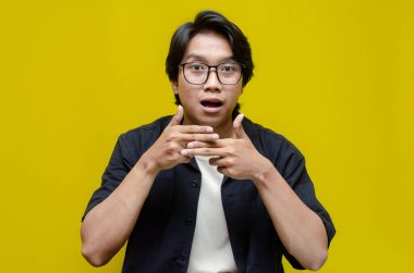 Siyah tişört giyen genç Asyalı adam sarı arka plan üzerinde işaret dili kullanıyor.. 
