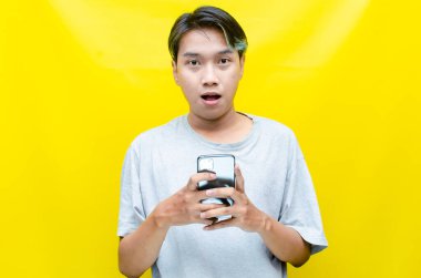 Sarı arka planda akıllı telefonu olan genç Asyalı adam. 