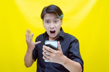 Sarı arka planda akıllı telefonu olan öfkeli Asyalı adam. 