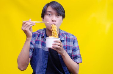 Asyalı adam sarı arka planda lezzetli eriştelerden hoşlanıyor. 