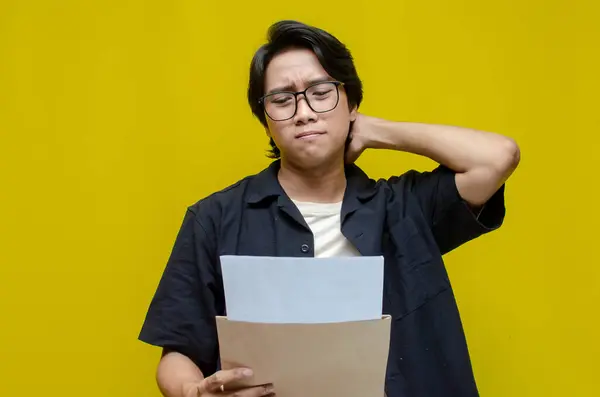 Düşünceli genç Asyalı adam sarı arka planda belgeler okuyor..