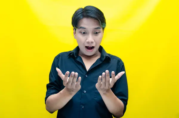 Sarı arka planda ellerine bakan duygusal Asyalı genç adamın portresi..