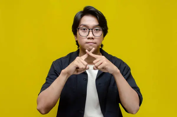 Siyah tişört giyen genç Asyalı adam sarı arka plan üzerinde işaret dili kullanıyor.. 