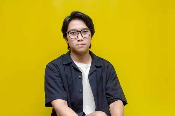 Sarı arka planda duran gözlüklü genç Asyalı adamın portresi..