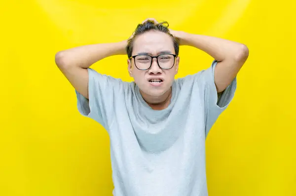 Sarı arka planda stresli Asyalı genç adam 