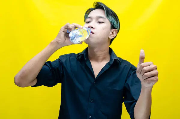 Genç Asyalı adam sarı arka planda su içiyor. 