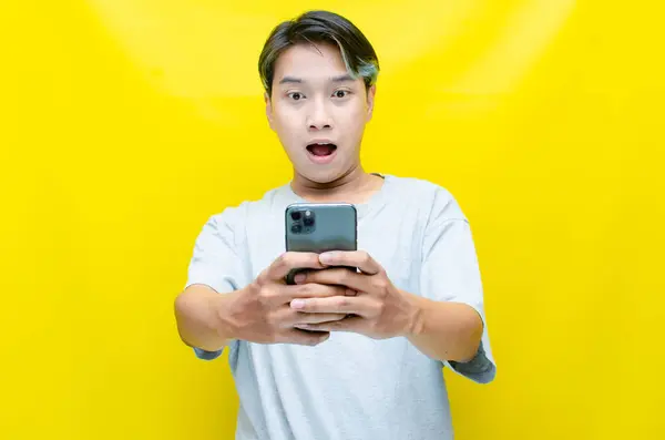 Sarı arka planda akıllı telefonu olan genç Asyalı adam. 
