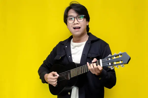 Gitar çalan şık Asyalı adam izole edilmiş sarı arkaplan