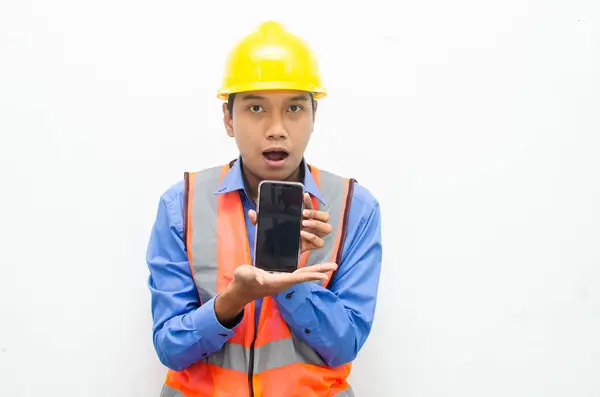 Asyalı inşaat işçisi sarı güvenlik kaskı takıyor ve telefonu tutuyor. 