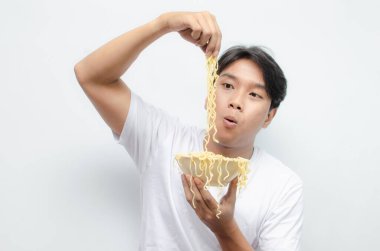 Genç yakışıklı Asyalı adam kaseden erişte çorbası içiyor ve çatal kullanarak büyütüyor. 