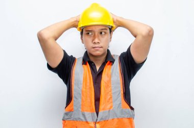 Sarı Miğferli ve Turuncu Yelekli Genç Asyalı İnşaatçı Düşünceli Hareket Ediyor. Derin düşüncelere dalmış, bir fikir arıyormuş. İfadesi düşüncelere dalmış. 