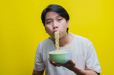 Günlük tişörtlü genç Asyalı Adam Aç İfadesiyle Yemek Yiyen ve Yutan Şehriye Çubuklarını Kullanıyor