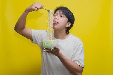 Asyalı Adam, onları çatalla kaldırarak bir kasede erişte yiyor. Krem rengi krem rengi tişörtlü genç Asyalı Çatallı Lezzetli Erişte Çorbası